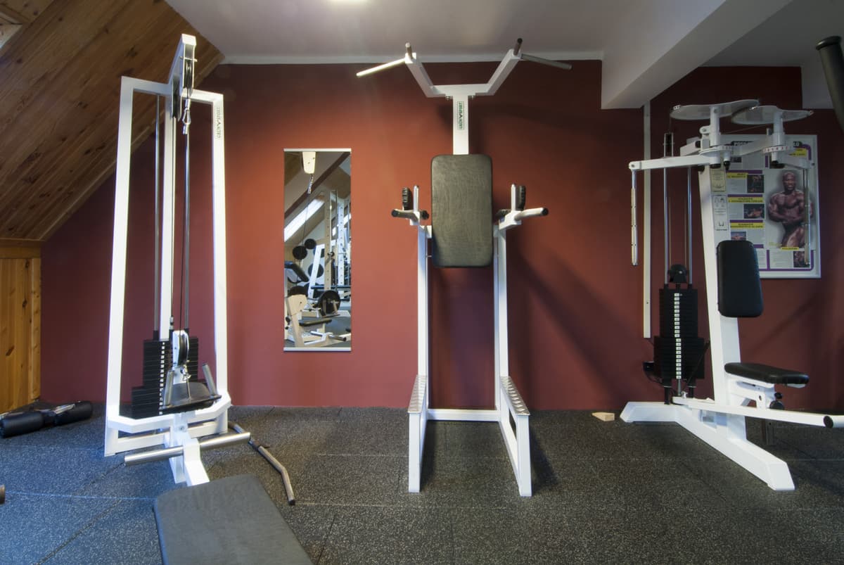 Teil des Fitnessraums mit einer Kraftmaschine, die eine Klimmzugstange und Gewichte hat.